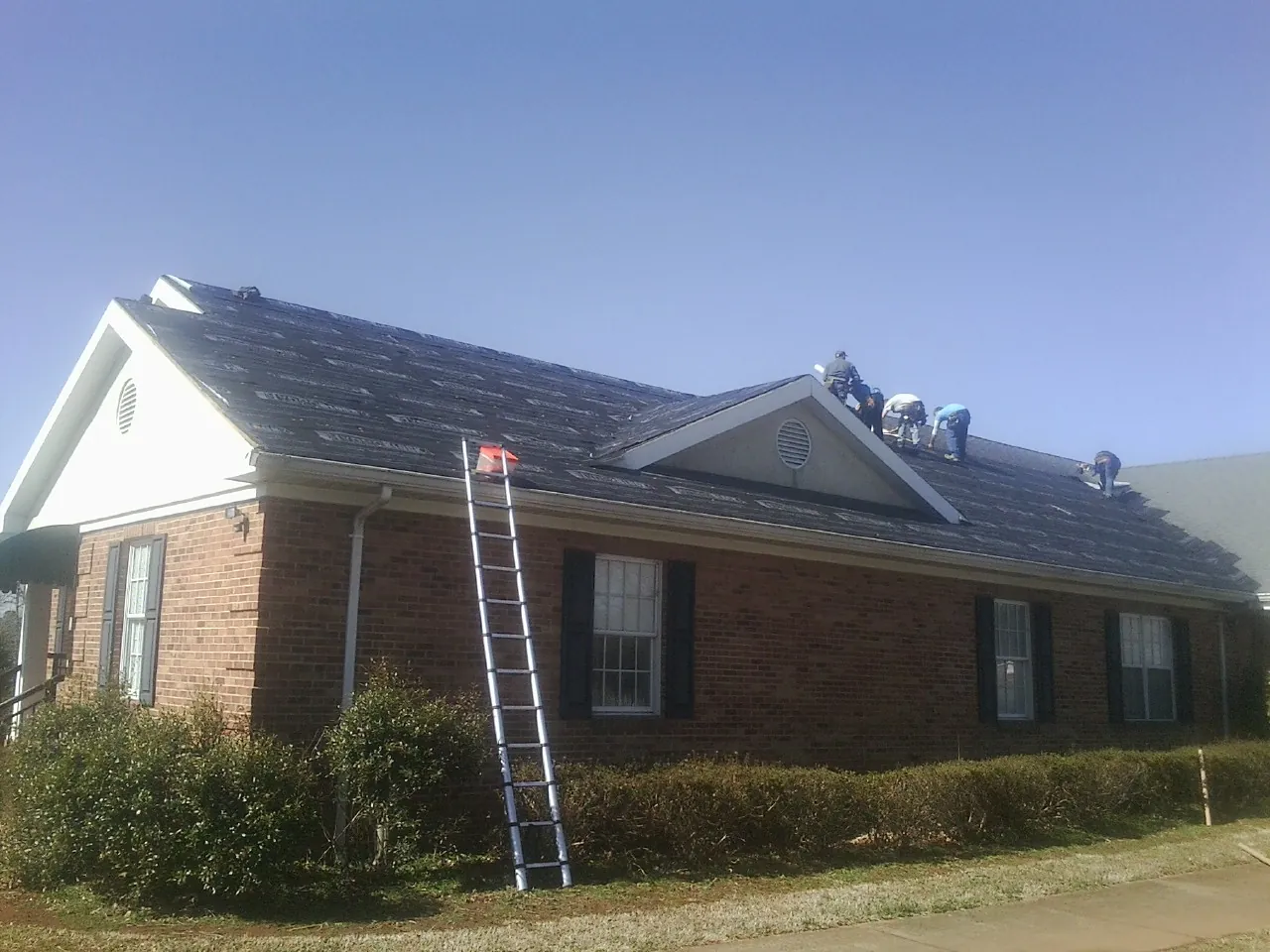 Crew tearing shingles off a brick ranch roof with a ladder set — Metal Roof Repair work by our crew in Oceanside