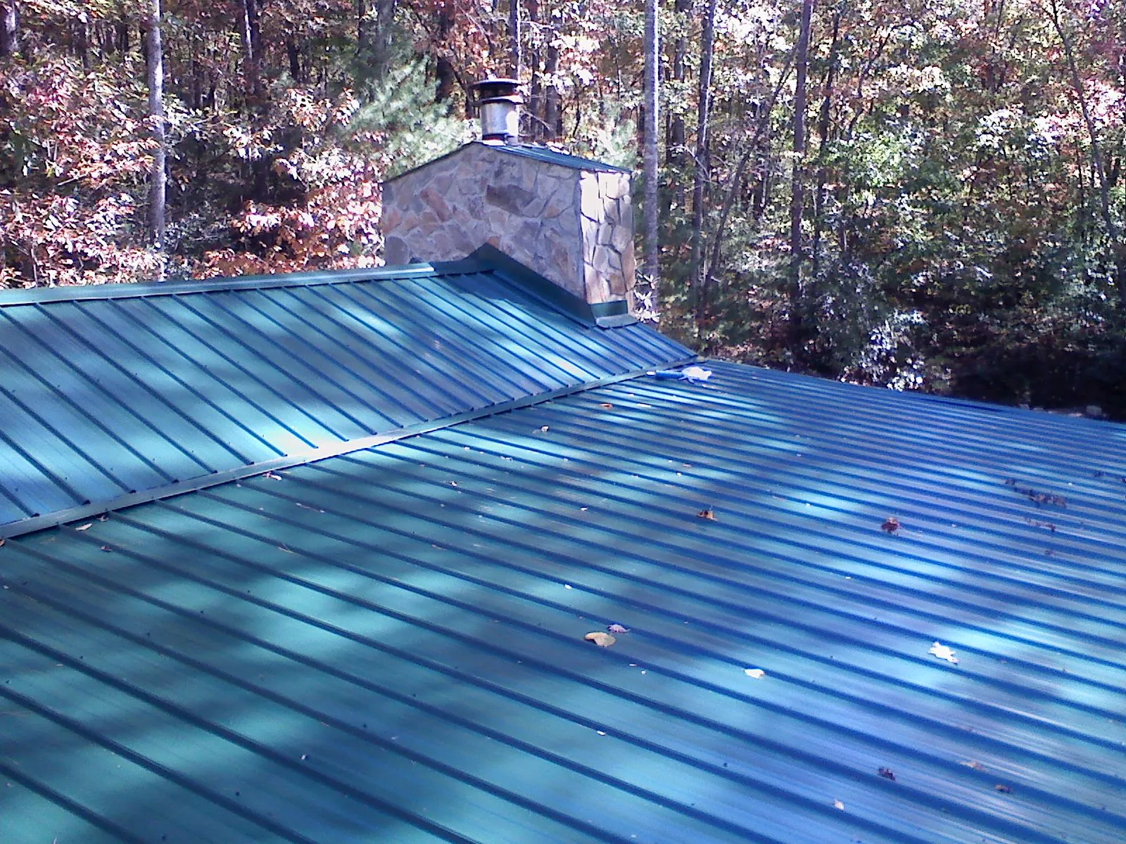New green metal roof and stone chimney surrounded by autumn woods in Oceanside